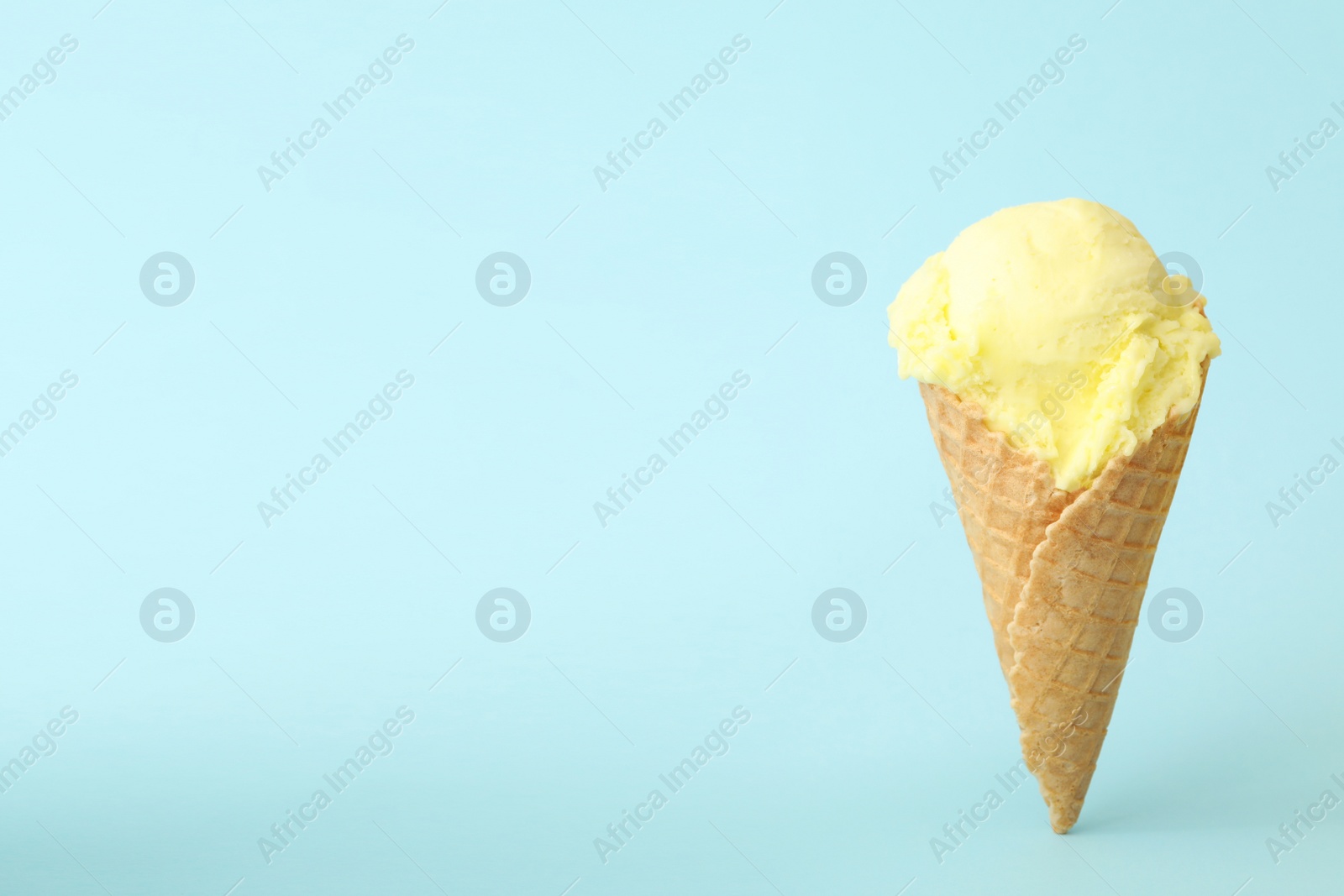 Photo of Delicious yellow ice cream in waffle cone on light blue background. Space for text