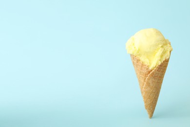 Delicious yellow ice cream in waffle cone on light blue background. Space for text