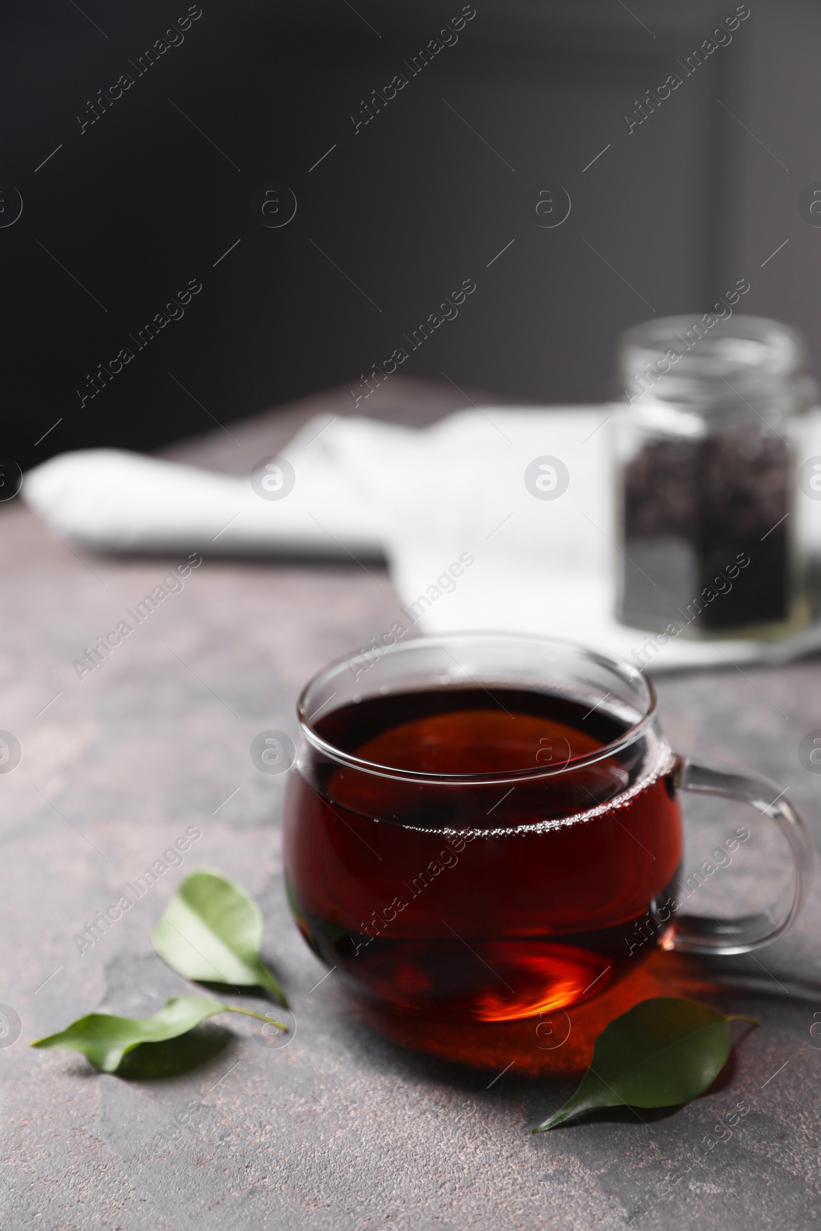 Photo of Tasty hot tea in cup and leaves on grey table, closeup