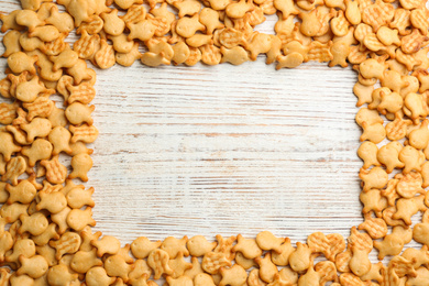 Frame of delicious goldfish crackers on white wooden table, flat lay. Space for text