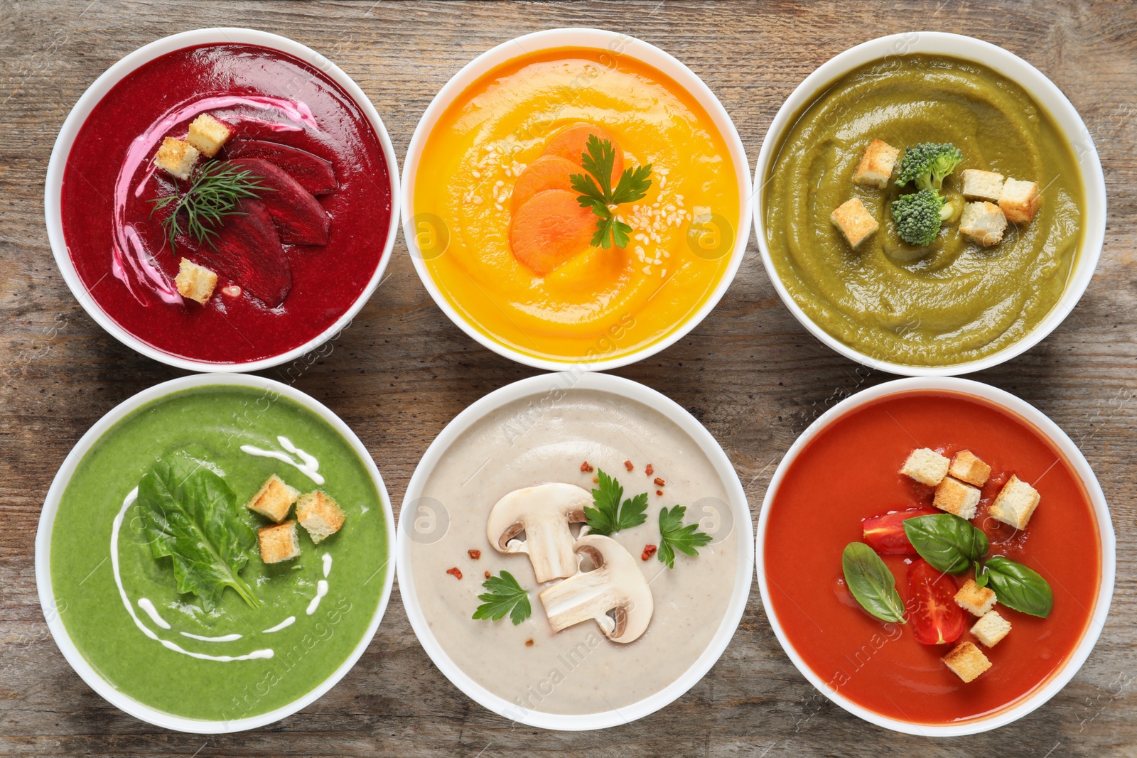 Photo of Various cream soups in bowls on wooden background, top view