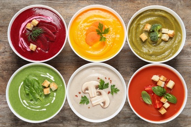 Photo of Various cream soups in bowls on wooden background, top view