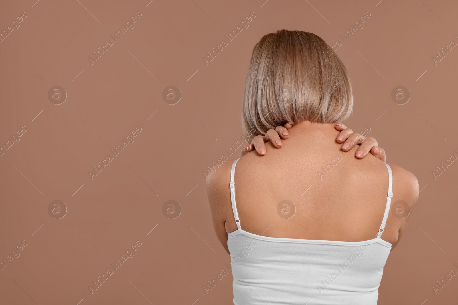 Photo of Woman suffering from pain in her neck on beige background, back view. Space for text