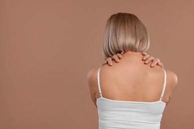 Photo of Woman suffering from pain in her neck on beige background, back view. Space for text