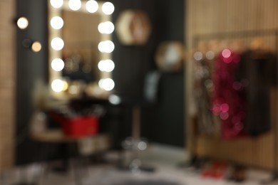 Blurred view of makeup room with stylish mirror near dressing table, chair and clothes rack