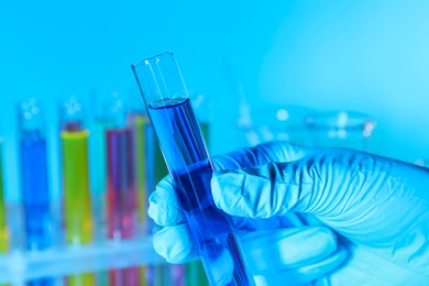 Photo of Scientist holding test tube with liquid on light blue background, closeup