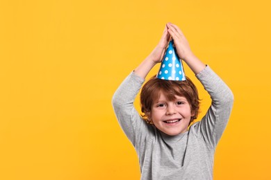 Photo of Birthday celebration. Cute little boy in party hat on orange background, space for text