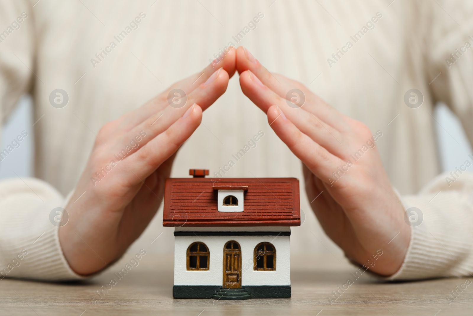 Photo of Home security concept. Woman covering house model at wooden table, closeup