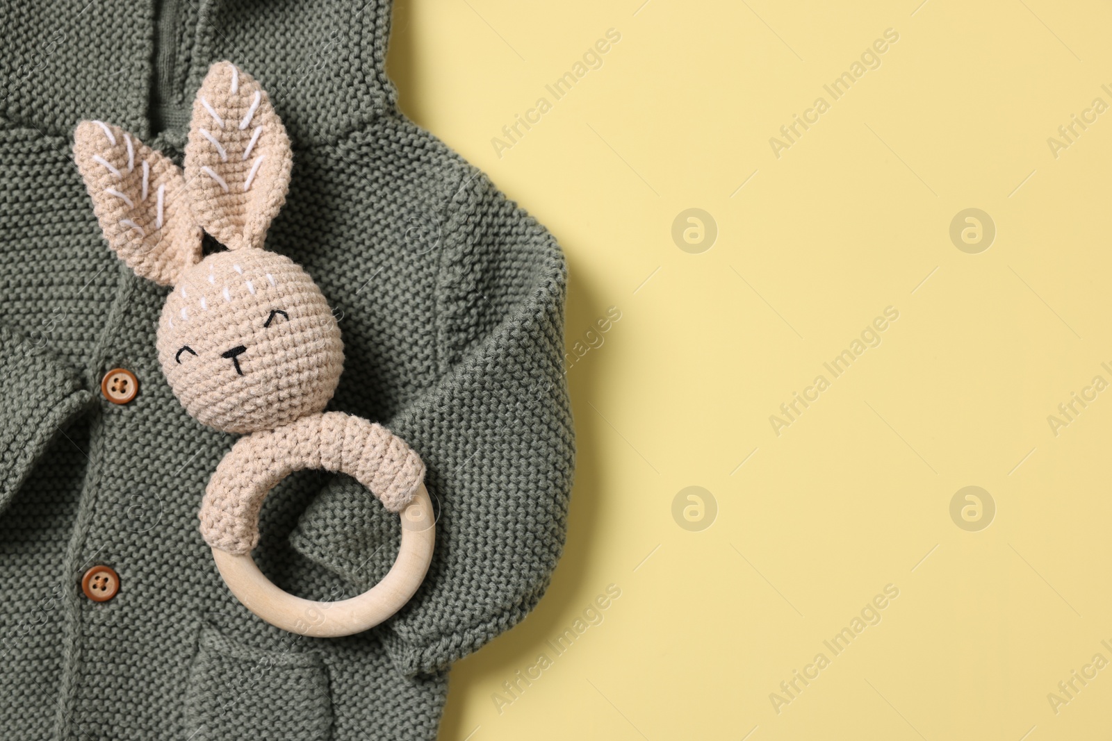 Photo of Baby accessories. Rattle and child's sweater on yellow background, top view. Space for text