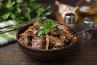 Tasty fried chicken liver with onion and fork on wooden table, closeup