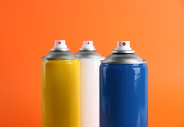 Photo of Colorful cans of spray paints on orange background, closeup
