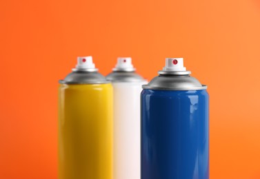 Colorful cans of spray paints on orange background, closeup