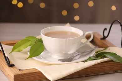 Photo of Cup of aromatic tea with milk, spoon, saucer and green leaves on table