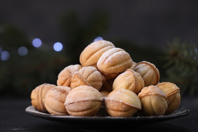 Photo of Plate of tasty nut shaped cookies with powdered sugar on black table, closeup