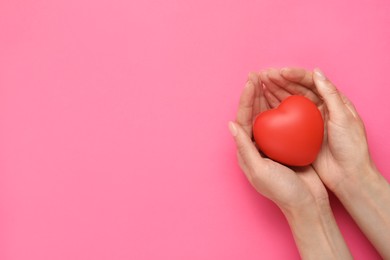 Photo of Woman holding red decorative heart on pink background, top view and space for text. Cardiology concept