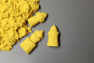 Castle figures made of yellow kinetic sand on grey background, flat lay. Space for text