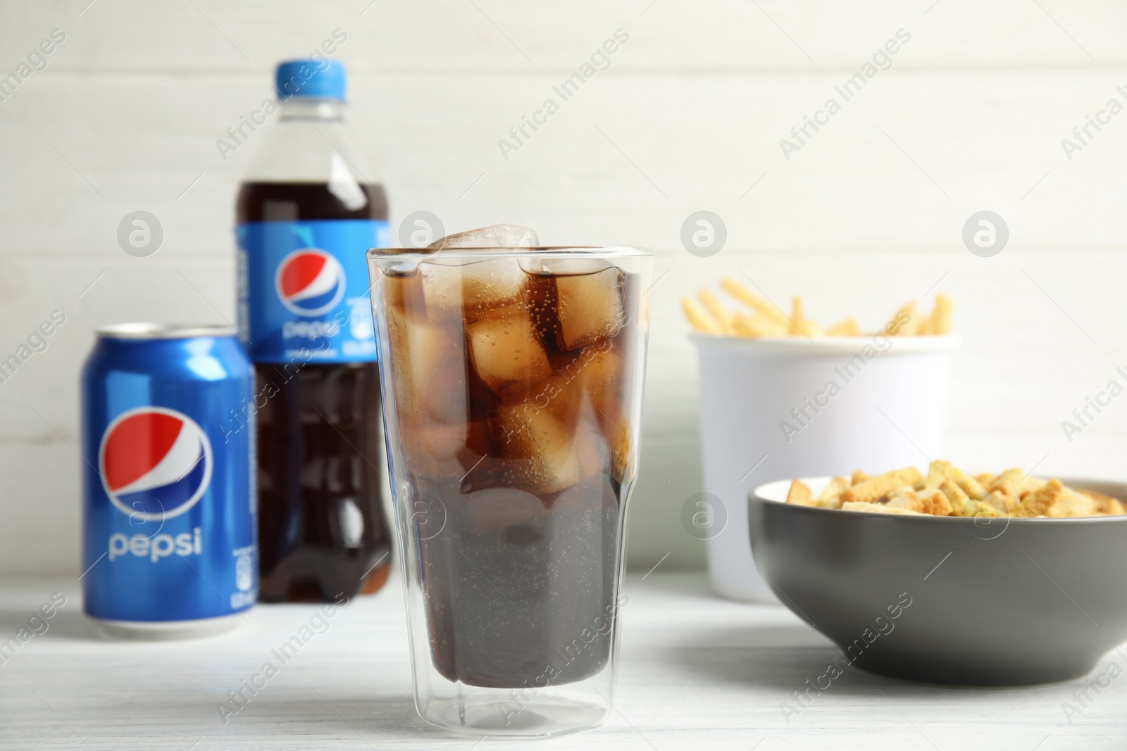 Photo of MYKOLAIV, UKRAINE - FEBRUARY 15, 2021: Glass of Pepsi and snack on white wooden table