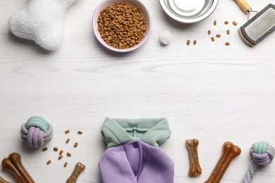 Photo of Flat lay composition with dog clothes, food and accessories on white wooden table. Space for text