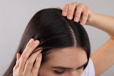 Woman examining her hair and scalp on grey background, closeup