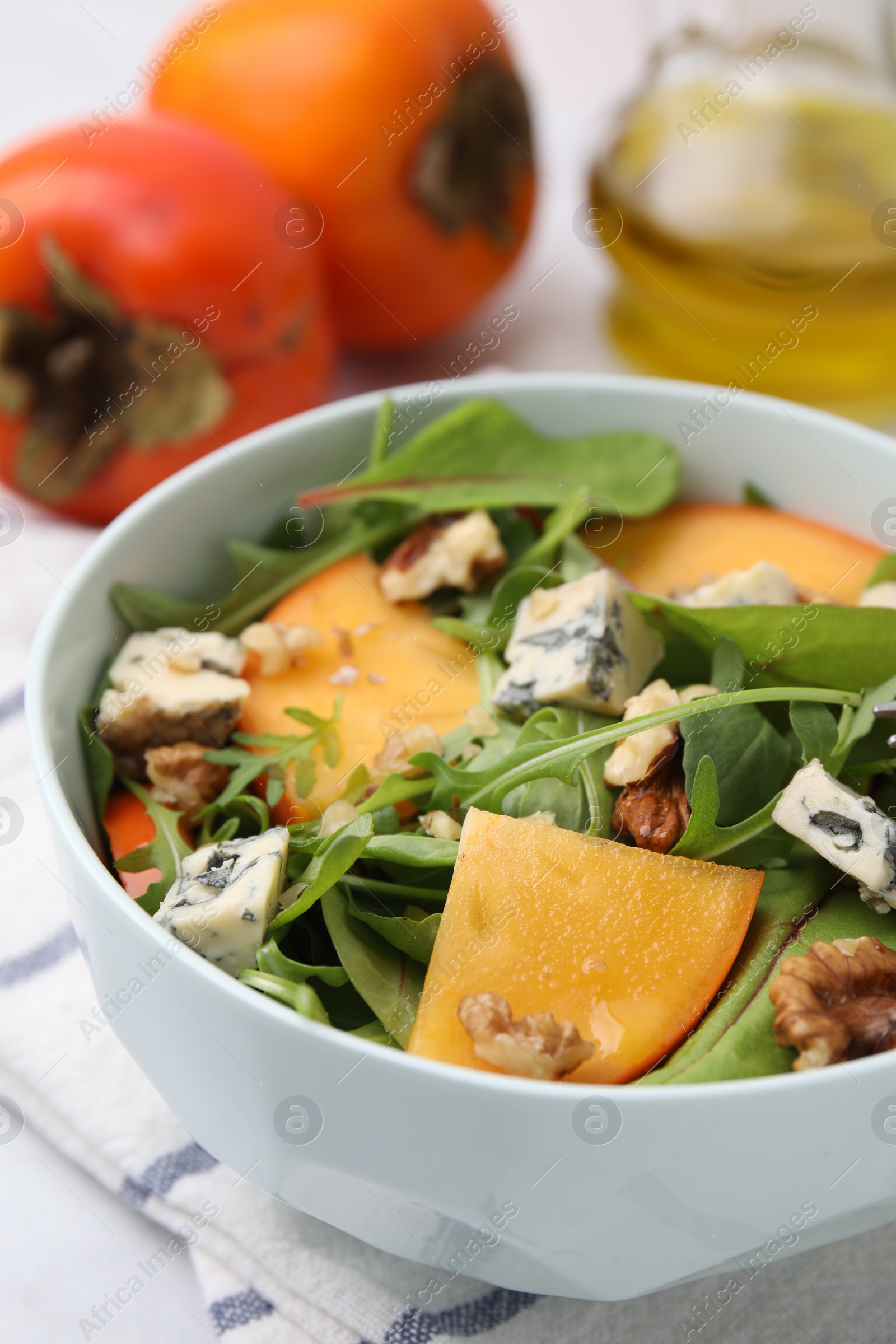 Photo of Tasty salad with persimmon, blue cheese and walnuts served on white table, closeup