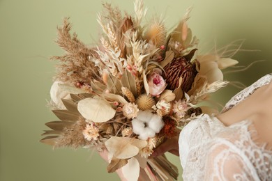 Photo of Bride holding beautiful dried flower bouquet on green background, closeup
