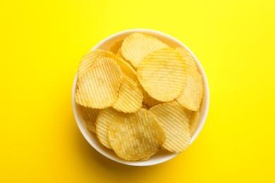 Photo of Delicious crispy potato chips in bowl on color background, top view