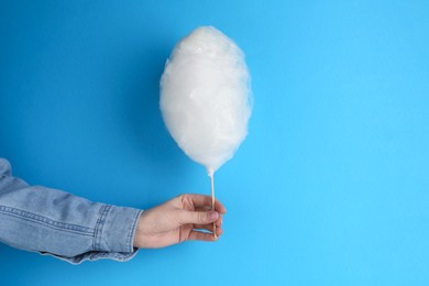 Woman holding sweet cotton candy on light blue background, closeup