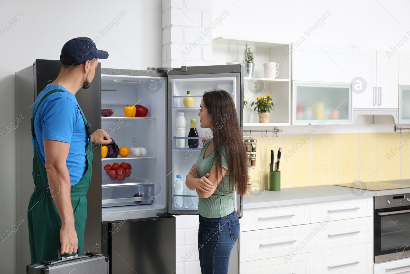 Photo of Male technician talking with client near refrigerator in kitchen