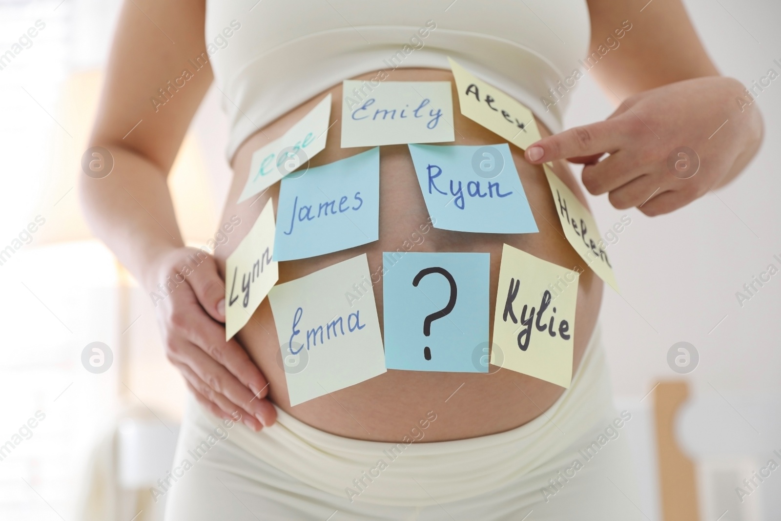 Photo of Pregnant woman with different baby names on belly indoors, closeup