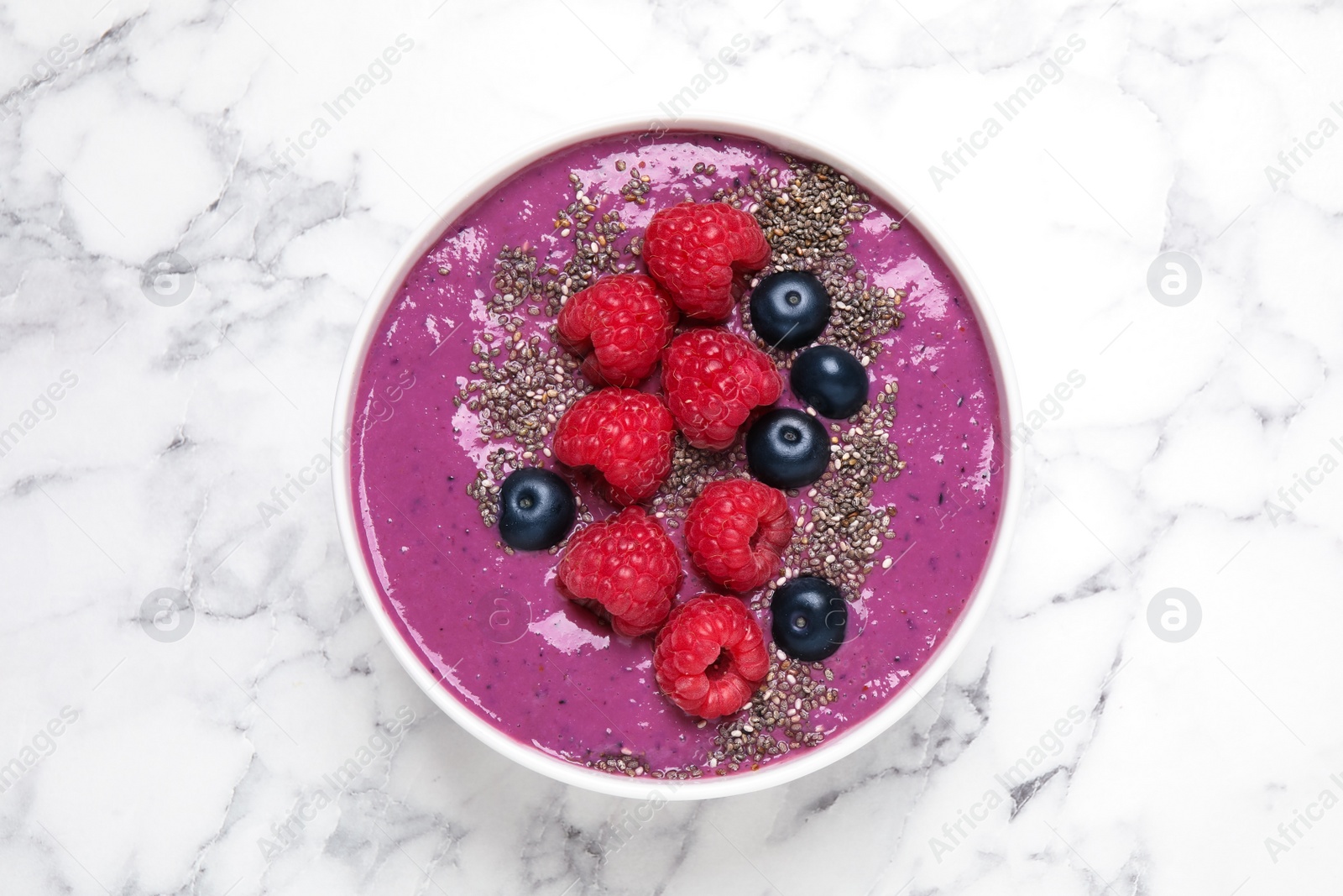 Photo of Delicious acai smoothie with raspberries and chia seeds on white marble table, top view