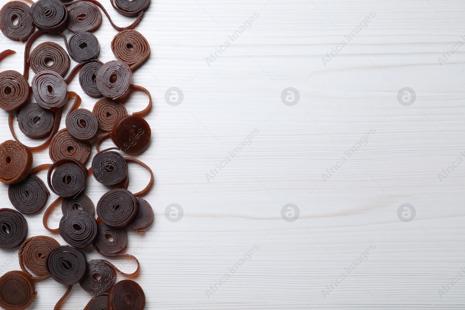 Photo of Delicious fruit leather rolls on white wooden table, flat lay. Space for text