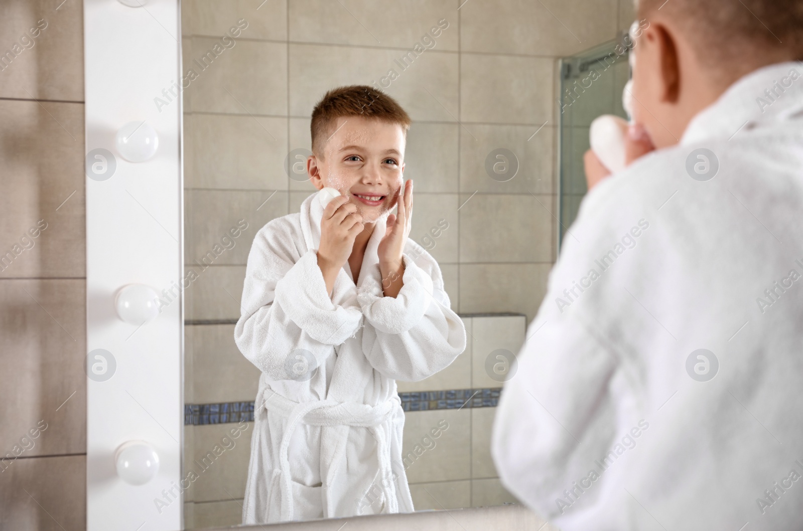 Photo of Little boy washing face with soap near mirror in bathroom