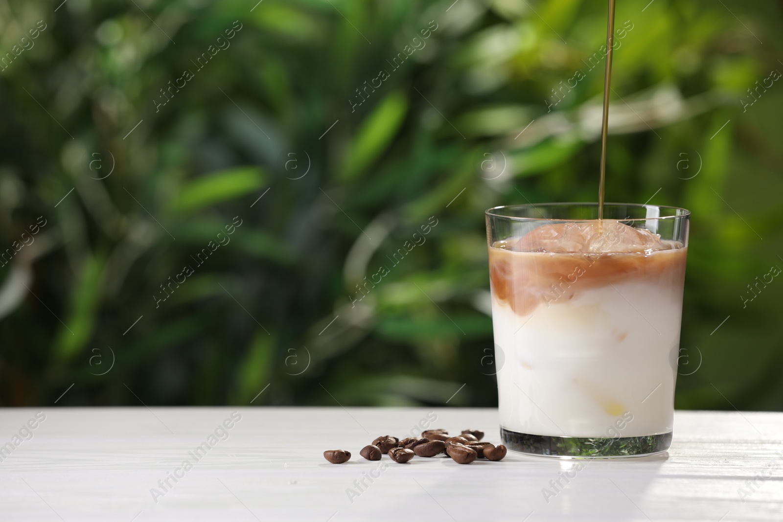 Photo of Making iced coffee at white wooden table outdoors, closeup. Space for text