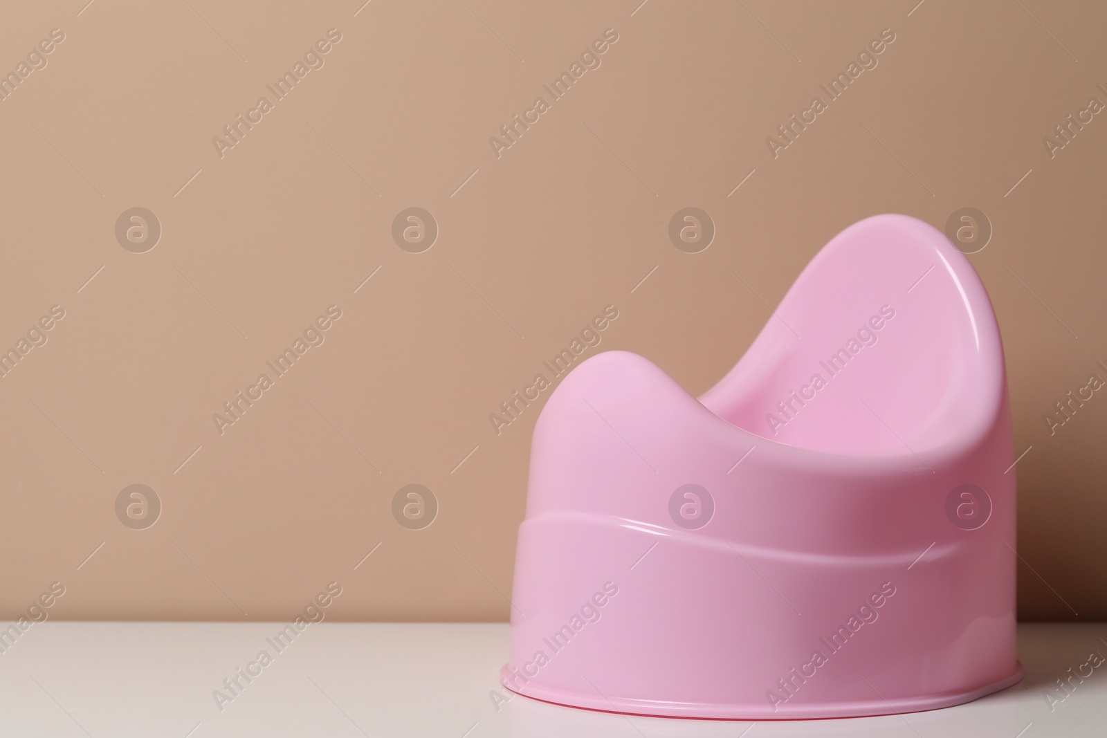 Photo of Pink baby potty on white table near brown wall, space for text. Toilet training