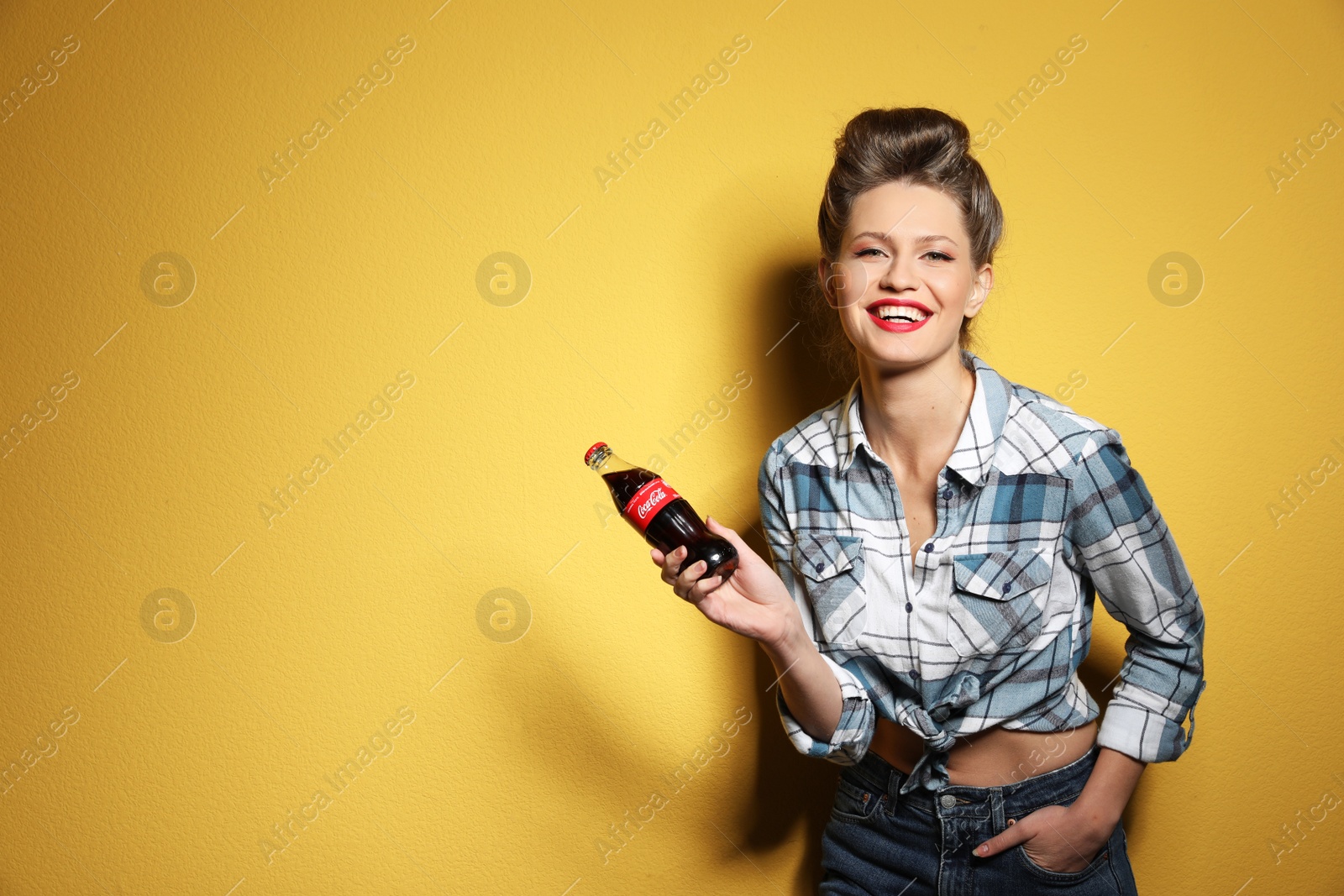 Photo of MYKOLAIV, UKRAINE - NOVEMBER 28, 2018: Young woman with bottle of Coca-Cola on color background, space for text