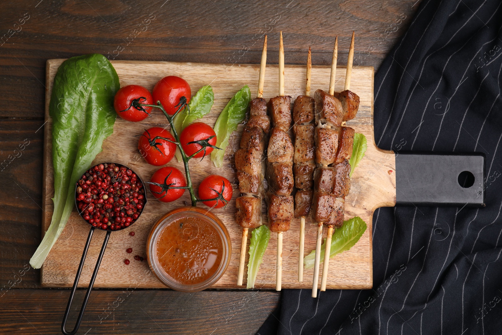 Photo of Tasty cooked marinated meat served with sauce and tomatoes on wooden table, flat lay