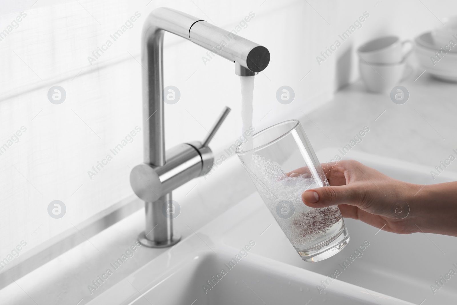 Photo of Woman filling glass with water from tap in kitchen, closeup