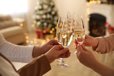 Photo of People clinking glasses of champagne in room decorated for Christmas, closeup. Holiday cheer and drink