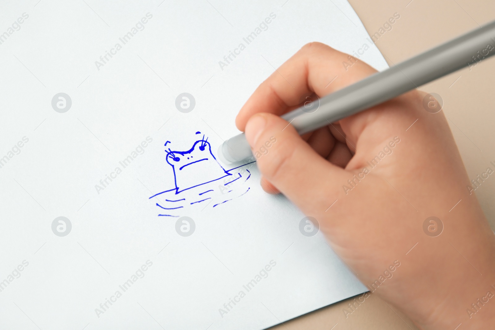 Photo of Child erasing drawing with erasable pen on paper sheet against beige background, closeup