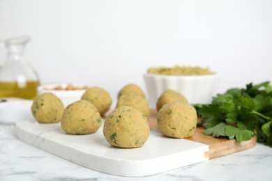 Photo of Raw falafel balls and parsley on white marble table. Space for text