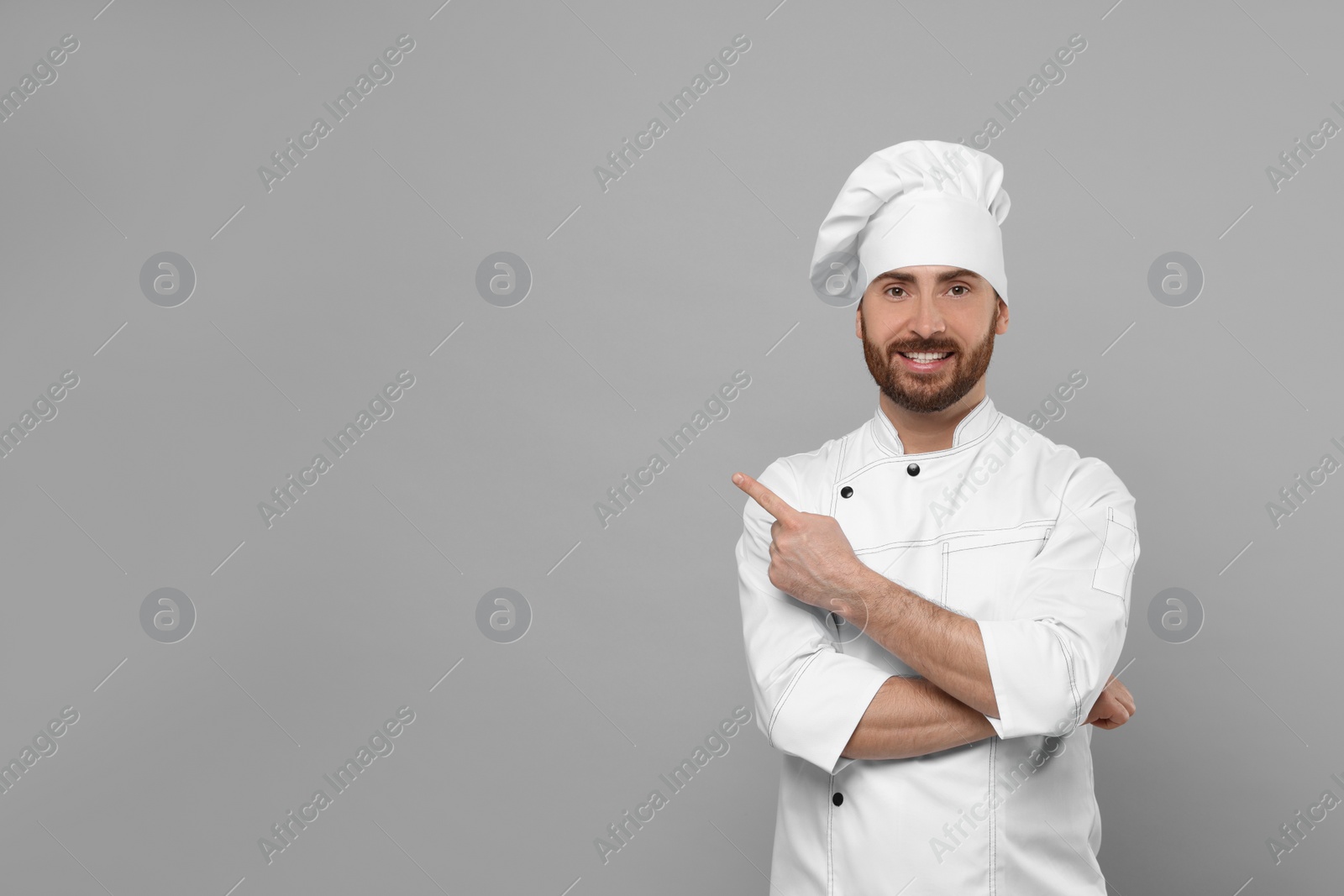 Photo of Mature chef pointing at something on grey background, space for text