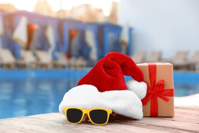 Photo of Authentic Santa Claus hat, gift box and sunglasses near pool at resort