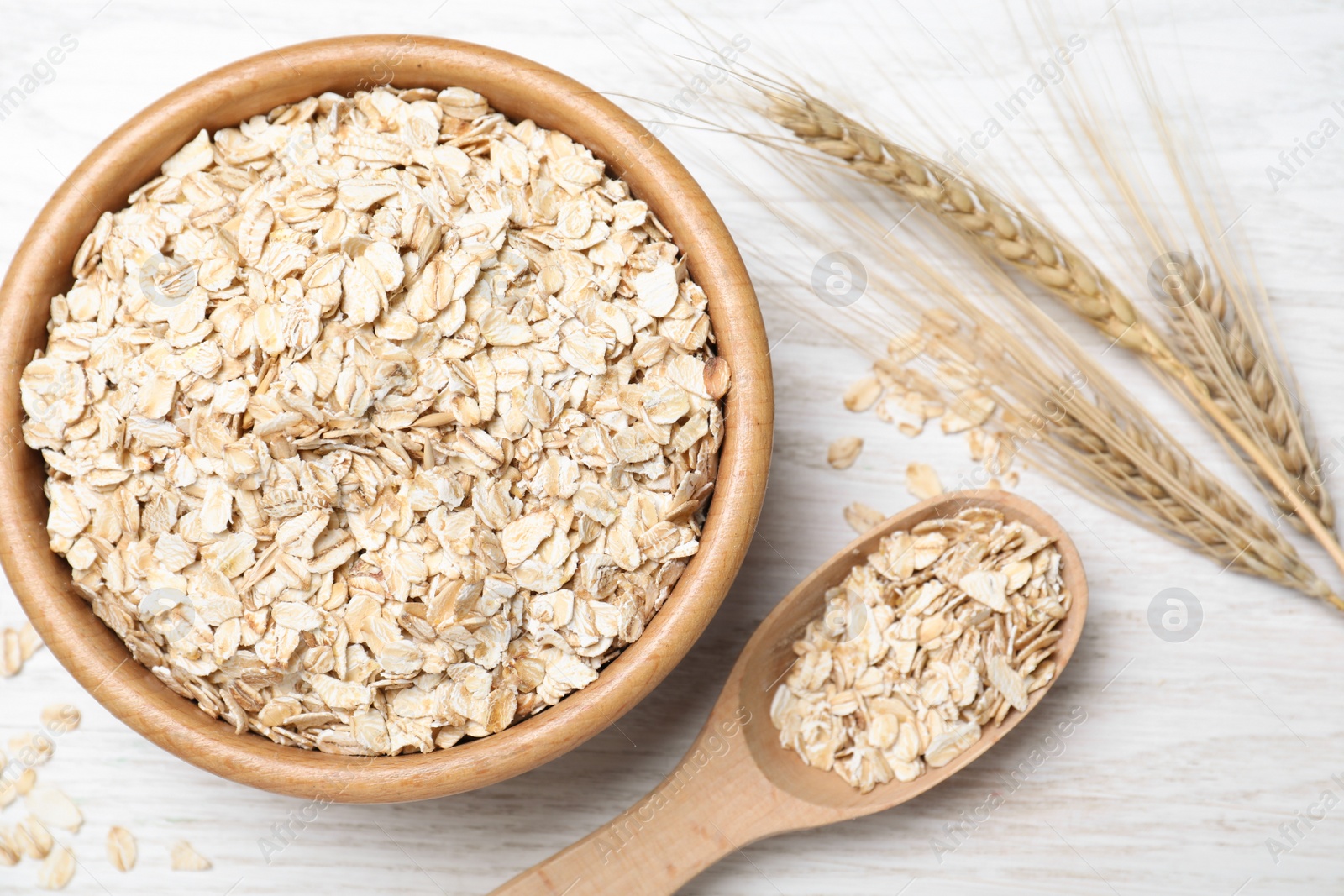 Photo of Oatmeal, bowl, spoon and spikelets on white wooden table, flat lay