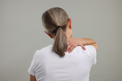 Photo of Mature woman suffering from pain in her neck on grey background, back view