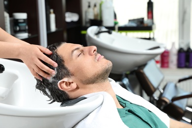 Stylist washing client's hair at sink in beauty salon