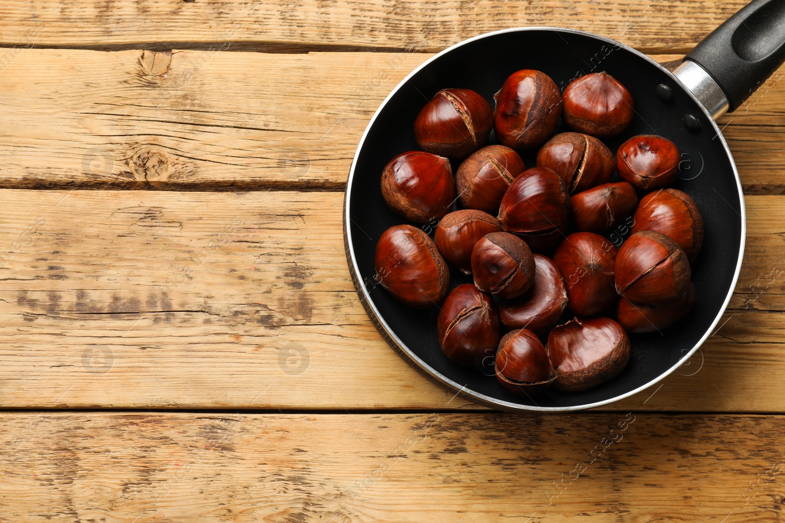 Photo of Fresh edible sweet chestnuts in frying pan on wooden table, top view. Space for text