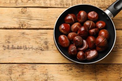 Fresh edible sweet chestnuts in frying pan on wooden table, top view. Space for text