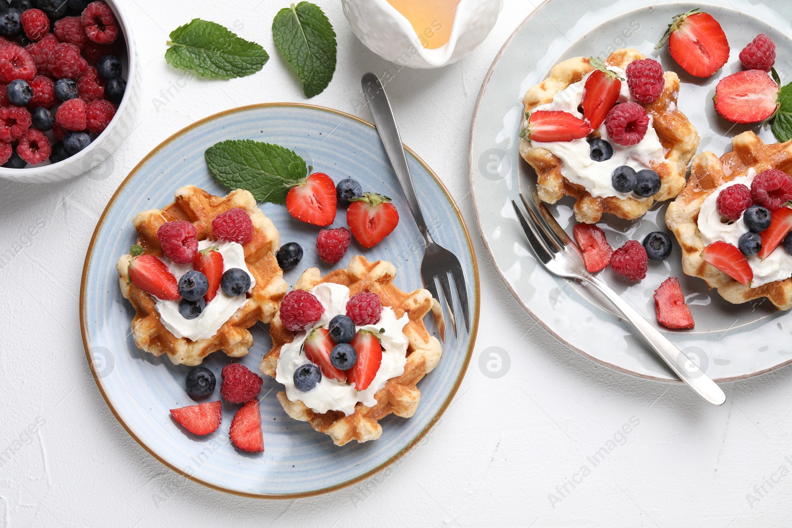 Photo of Delicious Belgian waffles with whipped cream and berries served on white table, flat lay