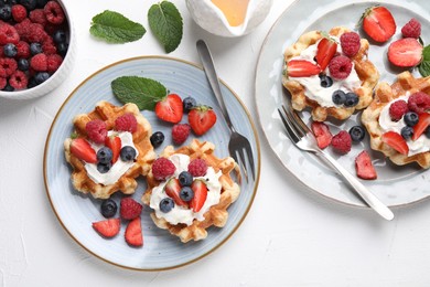 Delicious Belgian waffles with whipped cream and berries served on white table, flat lay