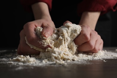 Photo of Making bread. Woman kneading dough at wooden table on dark background, closeup